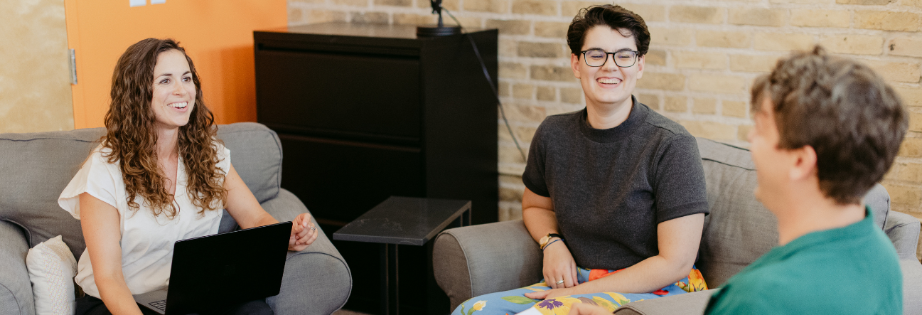 Photo of Sara McGarraugh, Alice Markey, and Nick Stilp sitting in grey chairs and talking. the background of the image is purple